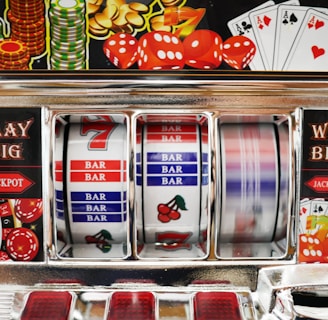 A close-up view of a slot machine with vibrant colors and various gambling symbols such as dice, coins, and playing cards. The reels display a combination of symbols, including bars, cherries, and the number seven. The chrome exterior and colorful details convey the theme of casino and gambling.