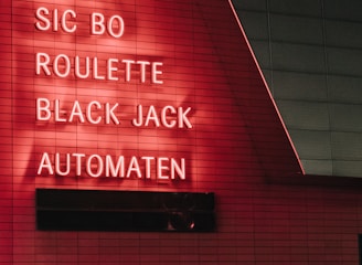Red neon letters are mounted on a dark tiled wall, displaying the words Poker, Sic Bo, Roulette, Black Jack, and Automaten.