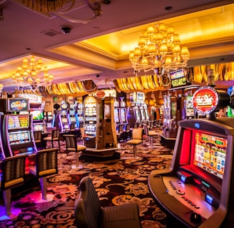 A vibrant casino interior filled with rows of colorful slot machines, each illuminated with bright lights and displays. The ceiling is adorned with elegant chandeliers and golden drapes, creating a luxurious atmosphere. The patterned carpet adds to the elaborate design of the space.