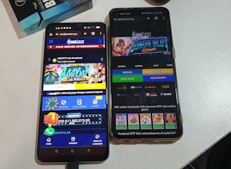 Two smartphones are displayed on a white surface, both showing gambling websites with colorful graphics, text, and various options for logging in and accessing games. The screens are bright and filled with promotional content related to casino and slot games.
